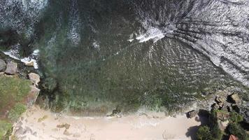 vista aérea superior das ondas quebram nas rochas em um oceano azul. ondas do mar na bela praia vista aérea drone 4k tiro. video