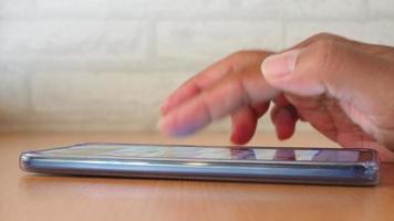 vista lateral de la mano del hombre usando un teléfono inteligente en una cafetería para buscar información