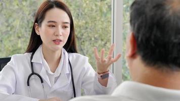 An Asian female doctor or nurse is using hands to explain information or something to a male patient in the health care center, focused on the female doctor. video