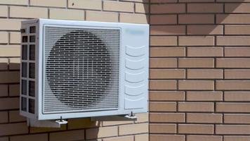 close-up van een moderne klimaatbeheersingseenheid tegen de achtergrond van een bakstenen muur van de gevel van het huis van buitenaf. muur airconditioning. luchtcompressor. video