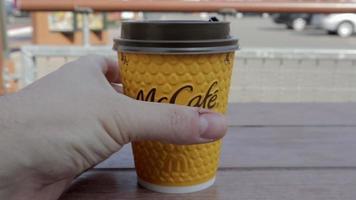 Closeup male hand takes McDonald's coffee in McCafe yellow paper cup. Takeaway food. A man drinks a hot coffee drink or tea in a fast food restaurant. Slow motion. Ukraine, Kiev - September 12, 2021. video