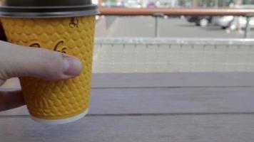 A man's hand puts coffee in a McCafe yellow paper cup on the table. Takeaway food. A man drinks hot coffee or tea at McDonald's fast food restaurant. Slow motion. Ukraine, Kiev - September 12, 2021.