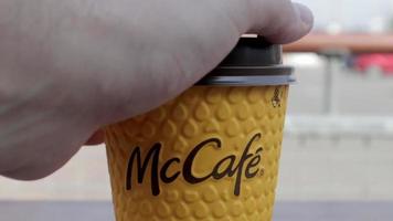 A man's hand opens a plastic lid drinker on a yellow paper coffee cup. Takeaway food. A man drinks hot coffee or tea at McDonald's fast food restaurant. Ukraine, Kiev - September 12, 2021.