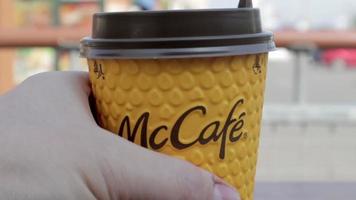 A man's hand puts coffee in a McCafe yellow paper cup on the table. Takeaway food. A man drinks hot coffee or tea at McDonald's fast food restaurant. Slow motion. Ukraine, Kiev - September 12, 2021.