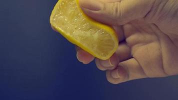 Hand squeezing half of lemon with lime drop on black background. video