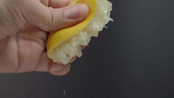 Hand squeezing half of lemon with lime drop on black background. video