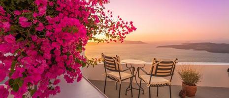 Beautiful view of Caldera and enjoying romantic scenery sunset Aegean sea, Santorini. Couple travel vacation, honeymoon destination. Romance with flowers, two chairs table and sea view. Luxury holiday photo