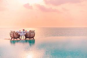 Seascape view under sunset light with dining table with infinity pool around. Romantic tropical getaway for two, couple concept. Chairs, food and romance. Luxury destination dining, honeymoon template