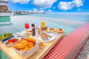 Breakfast in swimming pool, floating breakfast in tropical resort. Table relaxing in calm pool water, healthy breakfast and fruit plate by resort pool. Exotic summer diet luxury island beach lifestyle photo