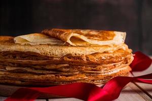 A stack of thin pancakes on a dark wooden background. A traditional dish of crepes for the holiday Maslenitsa.