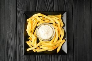 Fried French fries on a plate with sauce on a black wooden background. photo
