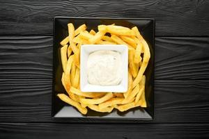 Fried French fries on a plate with sauce on a black wooden background. photo