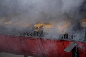 Handmade hamburger patties during the street food festival, smoke while cooking. photo