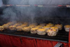 Handmade hamburger patties during the street food festival, smoke while cooking. photo