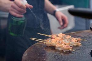 Cooking shrimp, prawn skewers on grill at street food festival - close up photo