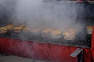 Handmade hamburger patties during the street food festival, smoke while cooking.