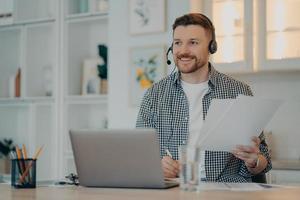 Happy man holding papers during online call at home photo