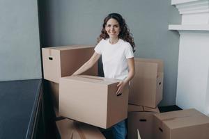 Happy woman is carrying box and smiling. Lady purchasing real estate and unpacking cardboard boxes. photo
