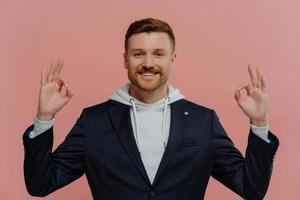 Happy redhead man making okay gesture isolated over pink wall photo