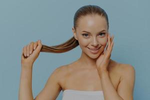 mujer joven naturalmente bonita que muestra un cabello de aspecto saludable y toca la piel limpia y brillante foto