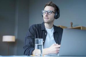 Young european man in wireless headphones listening audio podcast or watching webinar on laptop