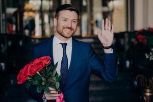 Young handsome man with neat beard in stylish tuxedo with red roses in his hand photo