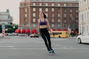 una foto completa de una mujer delgada y deportiva en paseos activos en cuchillas disfruta de la actividad física al aire libre durante las poses de los cálidos días de verano en un lugar urbano sobre asfalto. concepto de patinaje y ocio