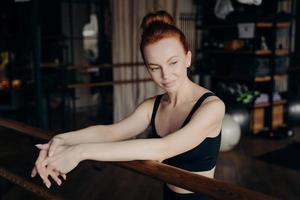 Pretty young red haired woman leaning on ballet barre photo