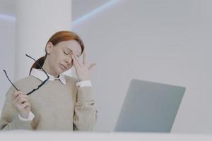 la empleada tiene dolor de cabeza, se toca los ojos y la frente. joven cansada en el escritorio de la oficina. foto