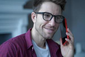 Young smiling german guy in glasses using mobile phone and talking on with friend photo