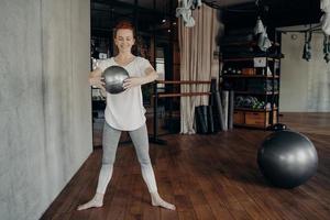 mujer joven en forma con el pelo rojo disfrutando de un entrenamiento de barra con una pequeña pelota de fitness foto