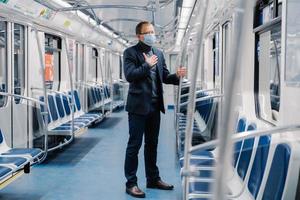 Coronavirus, Covid-19. Sick man feels unwell, has shortage of breathing, wears medical mask, poses in subway carriage, protects from contagious disease, avoids contact with people and viruses