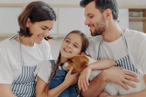 Happy lovely family smile and express sincere emotions, enjoy spending time together at cozy home. Smiling little child glad parent bought her new pet, cuddle jack russell terrier with love and care.