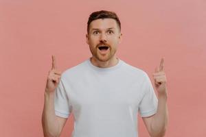 Excited young man pointing with two forefingers up and with shocked face expression photo