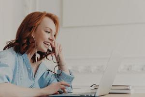 la foto de perfil de una mujer pelirroja feliz se ríe positivamente, se comunica en línea con un amigo, se toma un descanso después del trabajo, usa pantalones azul, posa en el espacio de coworking. gente, trabajo freelance, trabajo a distancia