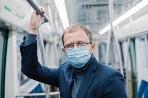 Coronavirus prevention. Man office worker wears transparent glasses, formal outfit, medical mask,ares about safety, poses in metro train, travels in public transport during Covid19 outbreak. photo