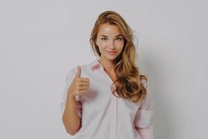 Enthusiastic young Caucasian woman keeps thumb up recommends something very good says yes photo