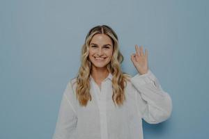 Joyful blonde woman making ok gesture with hand photo
