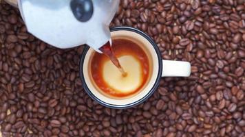 Video de 4k, sirviendo café negro en una taza. vista superior del espresso caliente vertido en una taza blanca de la cafetera de vapor géiser con fondo de granos de café. café con espuma