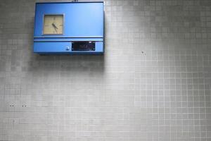 Bright blue retro clock on light gray wall and light. photo