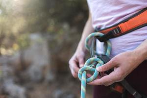 un escalador prepara equipo para escalar, mujer sostiene una cuerda, nudo