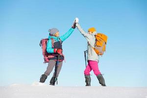 Two women walk in snowshoes in the snow, high five photo