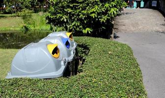 Row of plastic bins behind bush trees and beside concreate street in park. Three bins are used for waste separation in Bangkok, Thailand. photo