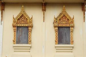 marco de color dorado y rojo de ventanas de madera pintadas de gris en la pared de color marrón claro en el antiguo estilo nativo tailandés en la pared de color amarillo claro en el templo en bangkok, tailandia. foto