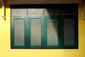 Row of retro dark green windows in rectangle shape and bright yellow wall of house in Thailand. Shadow and dust on surface of window. photo