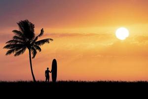 los surfistas de silueta escuchan en la playa con cocoteros por la mañana. foto