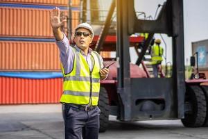 Young male engineer or manager wearing safety helmet and making hand to stop while talking on walkie talkie, transport and logistics concepts photo