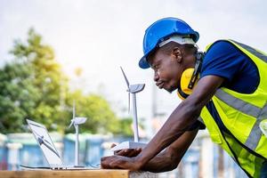 ingeniero ecológico escribiendo en una laptop y trabajando en un proyecto. en el escritorio hay modelos de molinos de viento. concepto de desarrollo sostenible foto