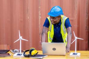 Ecology engineer typing on laptop and working on project. On desk are windmill models. Sustainable development concept photo