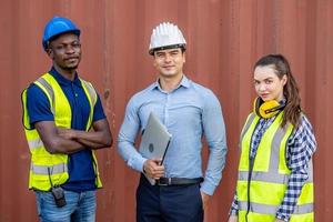 Confident foreman and engineers portrait in uniforms standing in front of the containers. Logistics and shipping, import and export concept photo
